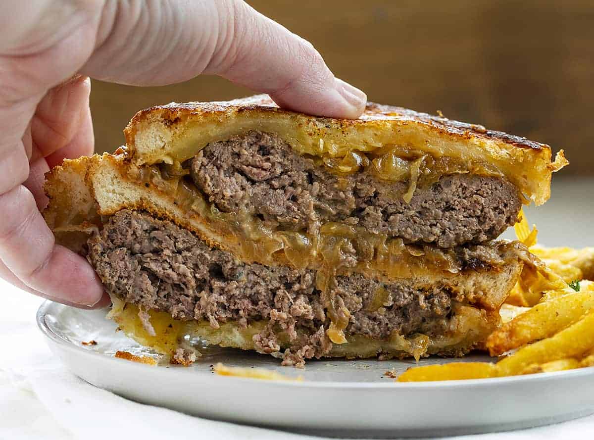 Hand Picking up a Double Decker Patty Melt on Plate with Fries