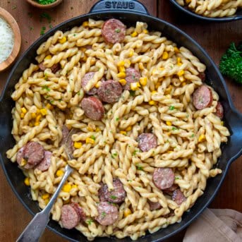 Skillet of Smoked Sausage Pasta on a wooden table with a spoon in it from overhead.