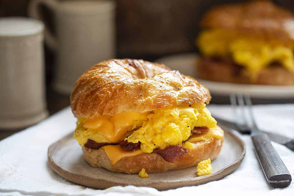 Bacon Egg and Cheese Croissant Sandwich on a Plate with Fork and Knife Next to It