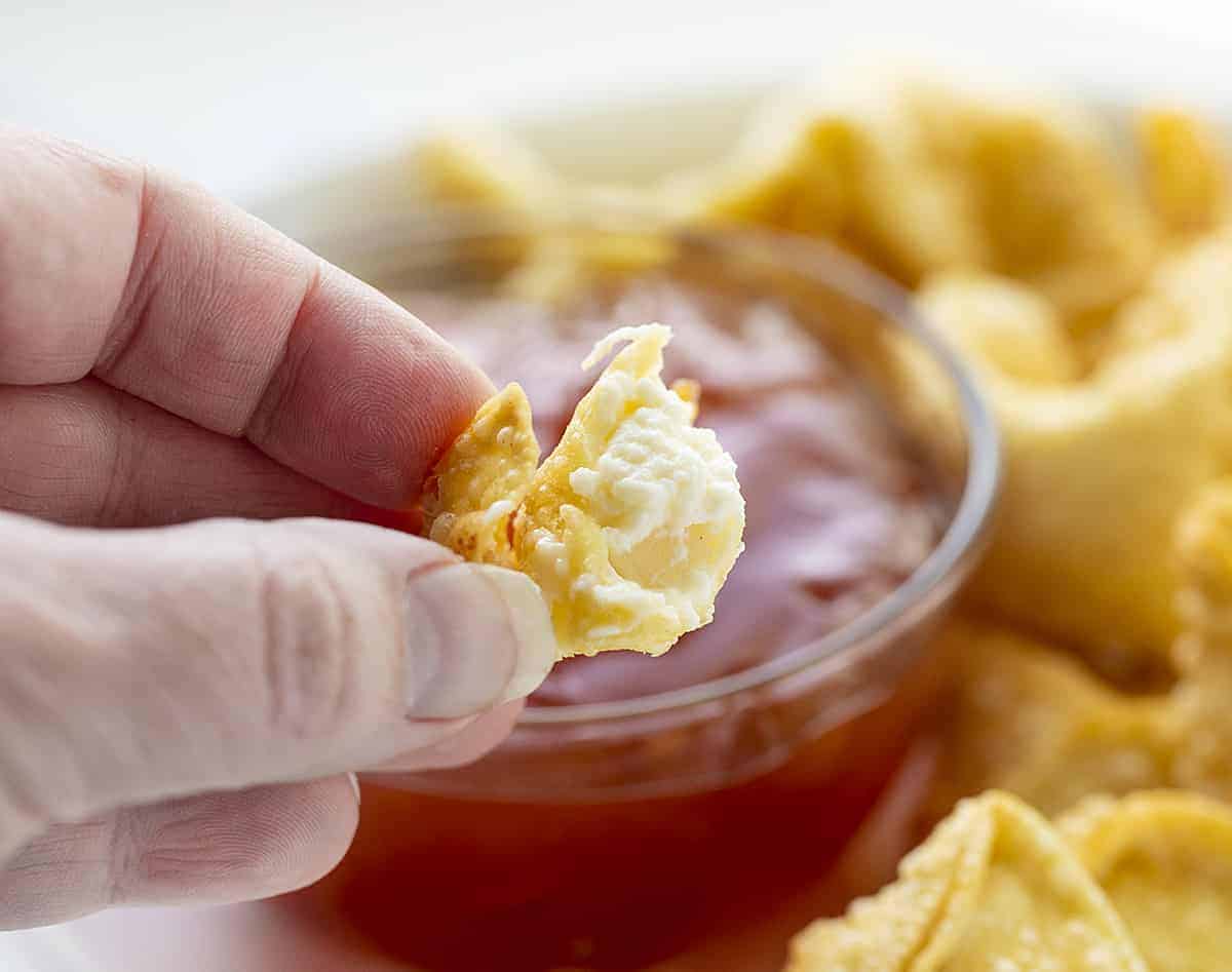 Hand Holding a Bit Into Cream Cheese Wonton Showing the Cream Cheese Inside