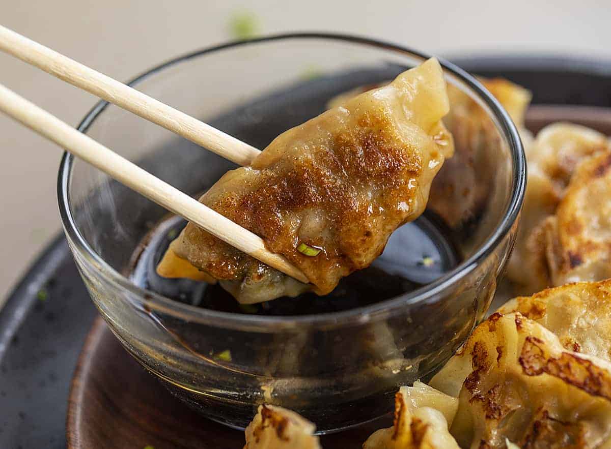 Chopsticks Picking Up a Fried Potsticker and Dipping in Sauce