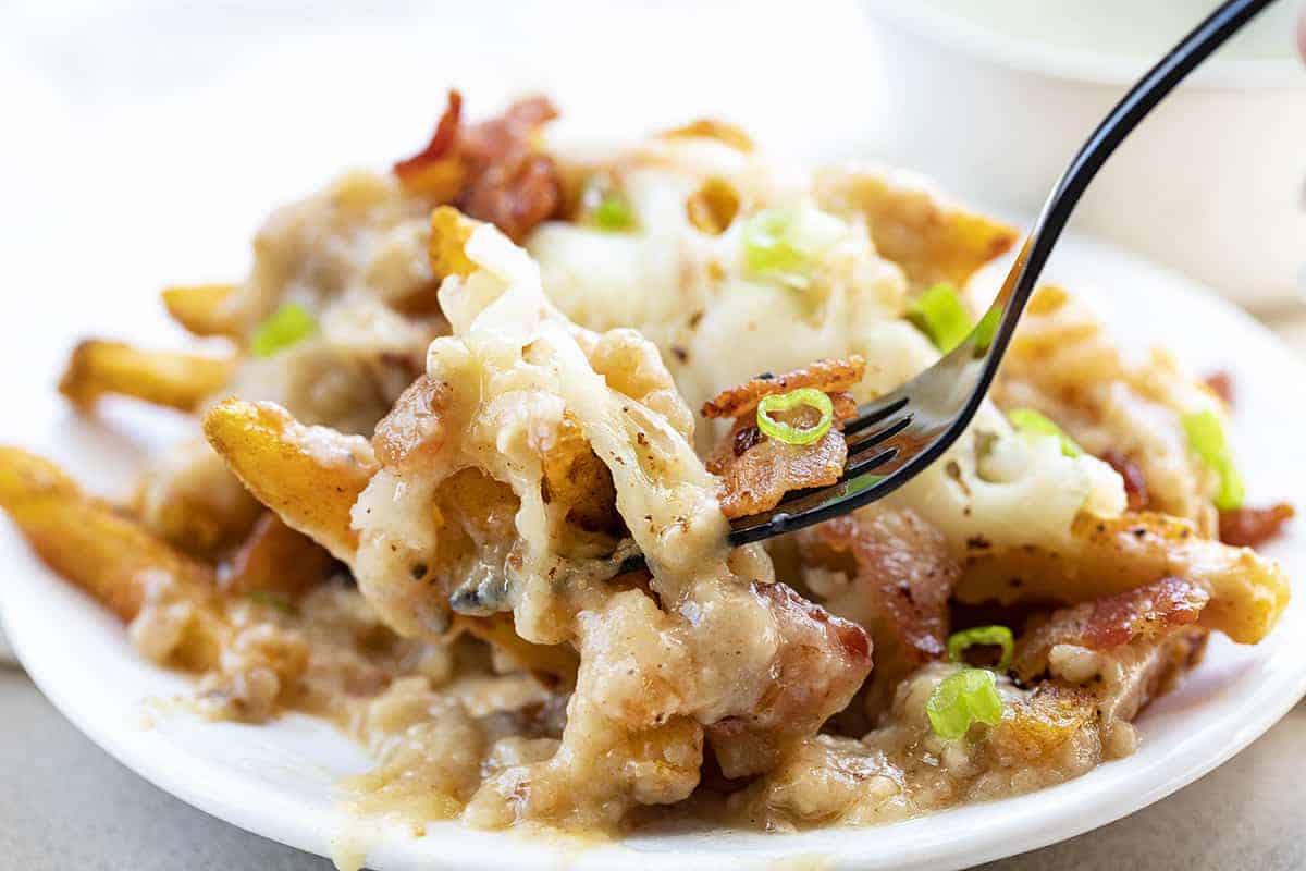 Plate of Poutine Soaked in Gravy and Fork Picking Up a Bite