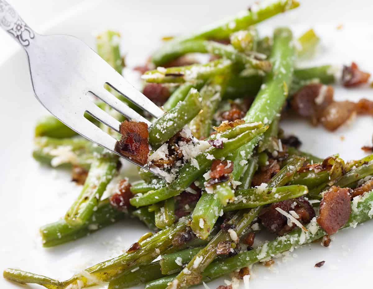 Forkful of Spicy Green Beans with Bacon and Cheese on White Plate