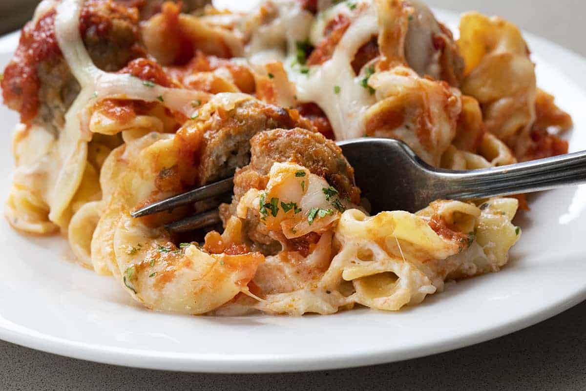 Fork Cutting Into Spaghetti Sauce Covered Meatball with Cheesy Noodles