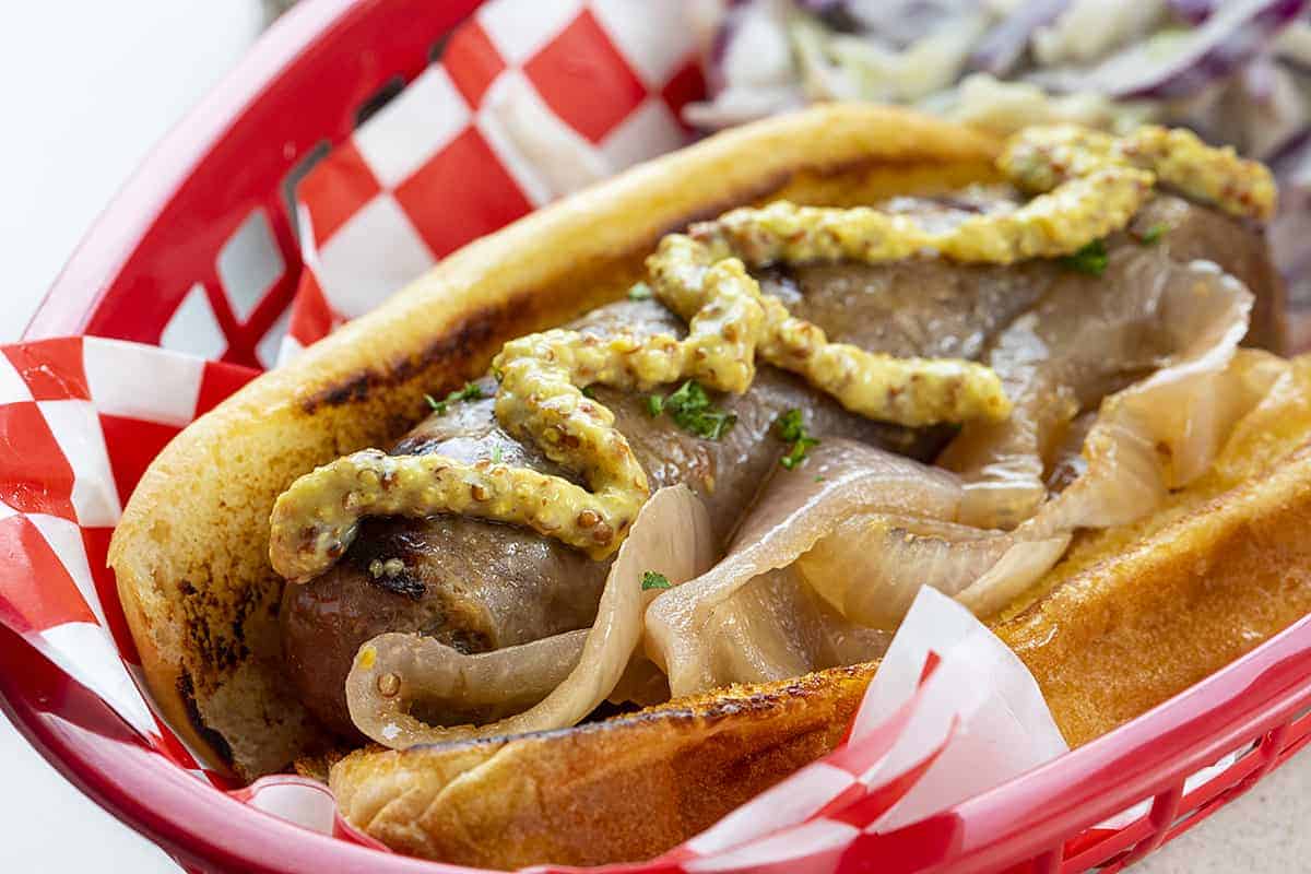 Close up of Root Beer Brat with Onions and Grainy Mustard in Red Basket