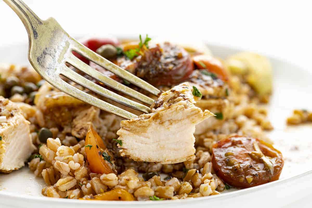 Fork Holding up a Piece of Tuscan Chicken from a White Plate