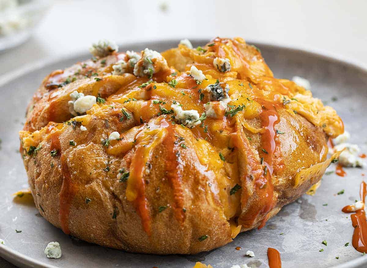 One Buffalo Chicken Pull Apart Bread on a Metal Plate Sprinkled with Blue Cheese and Hot Sauce