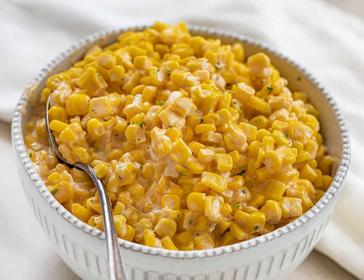 Big Bowl of Crockpot Cheesy Corn with a Serving Spoon and White Towel in the Background