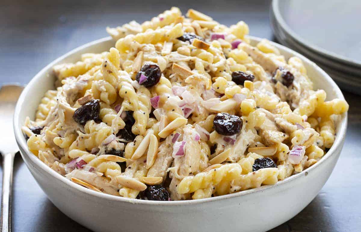 Cherry Chicken Pasta Salad in a White Bowl with Plates in Background