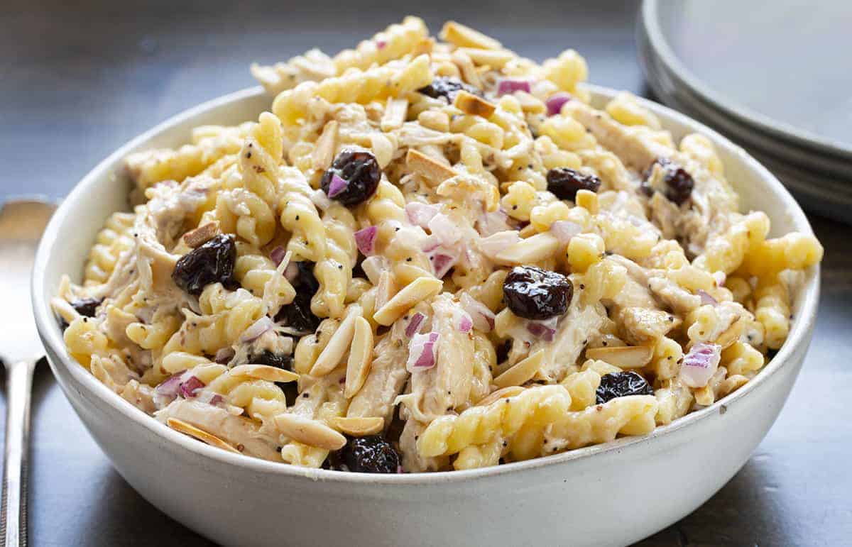 Insalata di pasta di pollo alla ciliegia in una ciotola bianca con piatti in background