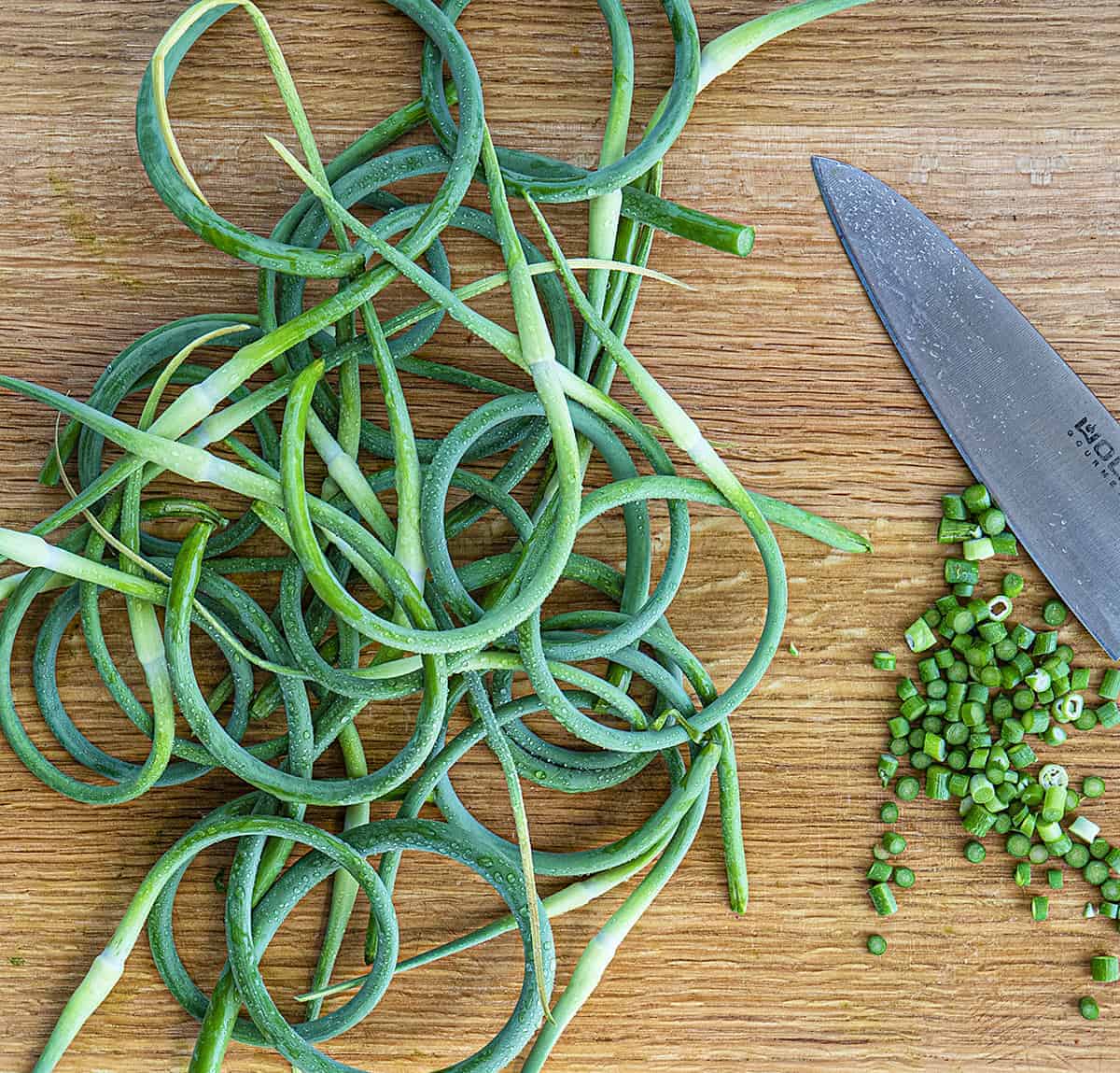 Overhead Image of Garlic Scapes with some Chopped Next to a Knife