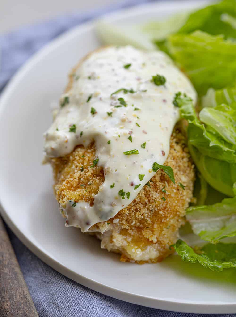 Very Close Vertical Image of Chicken Cordon Bleu on White Plate with Lettuce on Blue Napkin