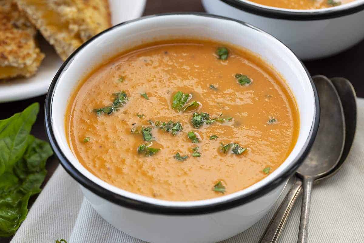 Roasted Tomato Soup in white Bowl with Black Rim and Grilled Cheese in the Back