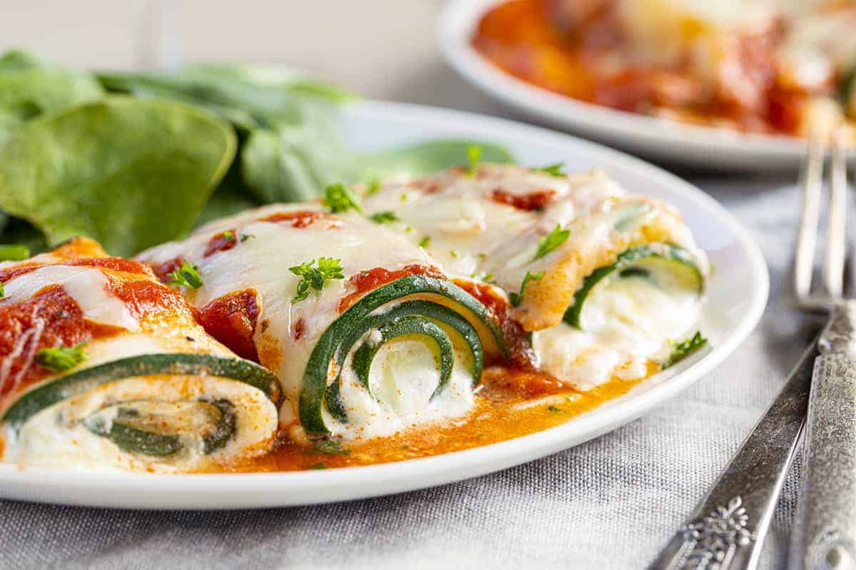 Three Five Cheese Zucchini Roll Ups on a White Plate With Filling Spilling Out