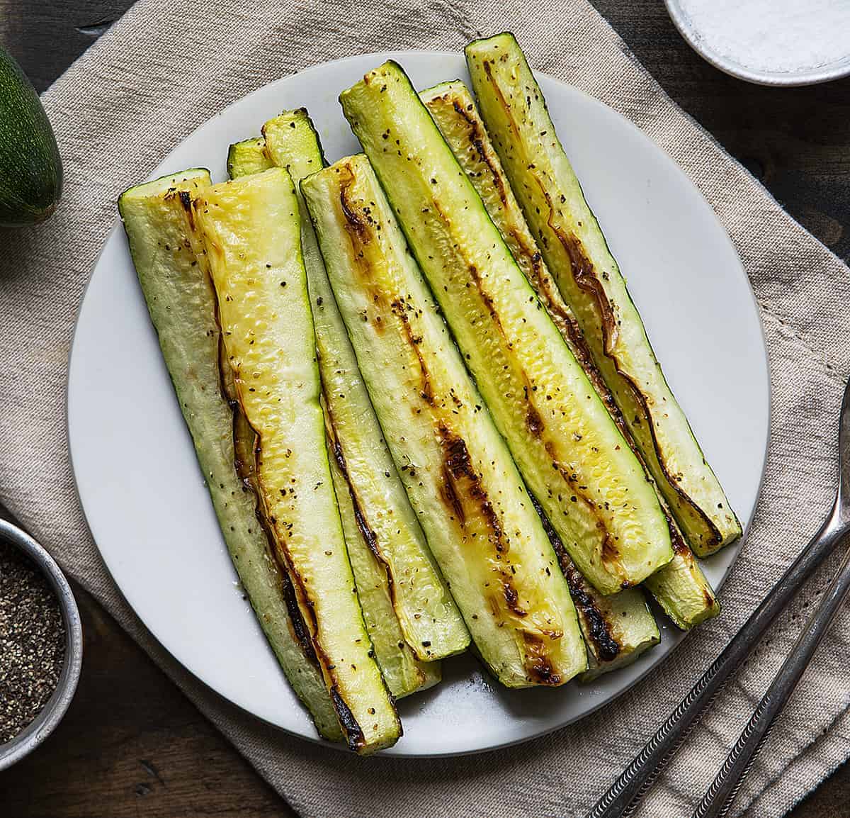 Overhead Image of Roasted Zucchini Spears on White Plate on Tan Napkin