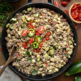 Skillet of Summer Goulash with a wooden spoon in the pan on a wooden table from overhead.