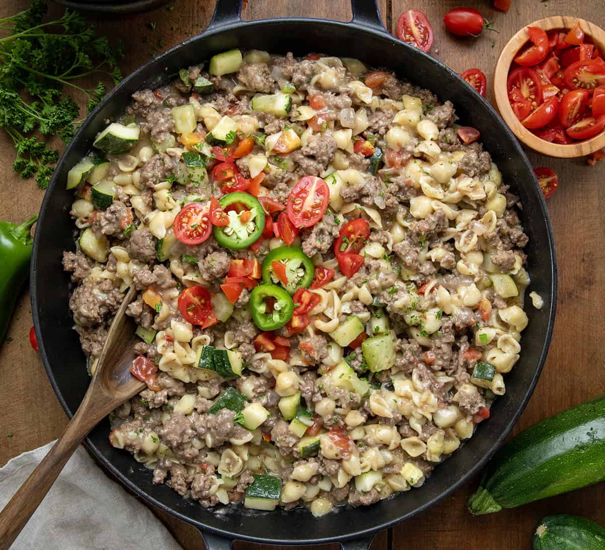 Summer Goulash is a hearty dish that is full of meat and lots of garden vegetables with pasta noodles that make this a filling meal that is the perfect recipe to use up your summer veggies! Skillet of Summer Goulash with a wooden spoon in the pan on a wooden table from overhead.