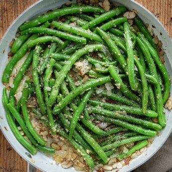 White Pan of Green Beans Almondine on a Wooden Cutting Board.
