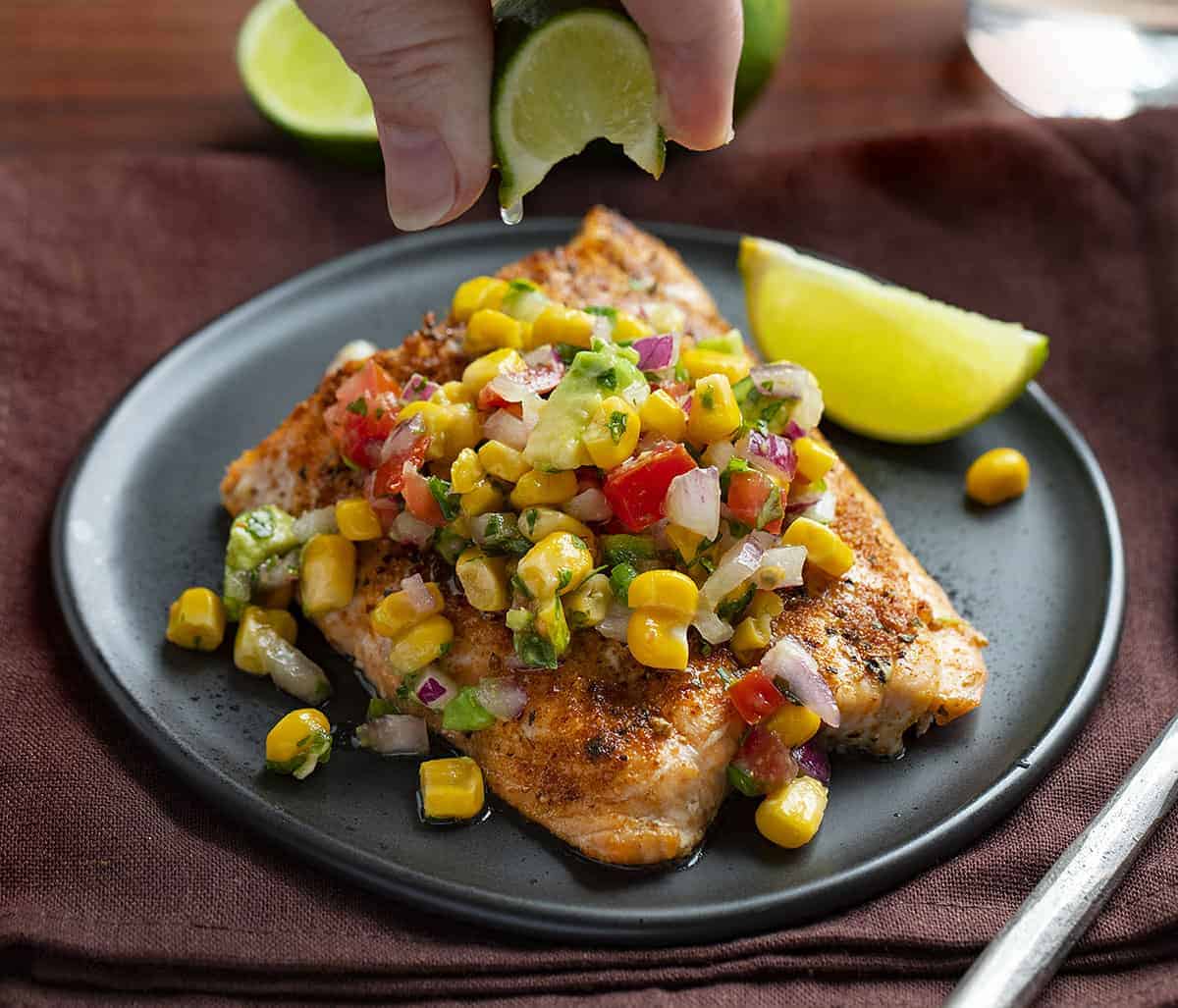 Adding Lime to Blackened Salmon covered in Avocado Corn Salsa