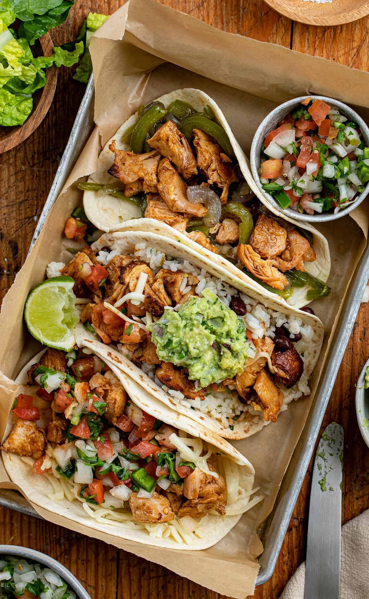 Overhead image of 3 kinds of Chicken Tacos - Chipotle Copycat Recipe in a pan with condiments