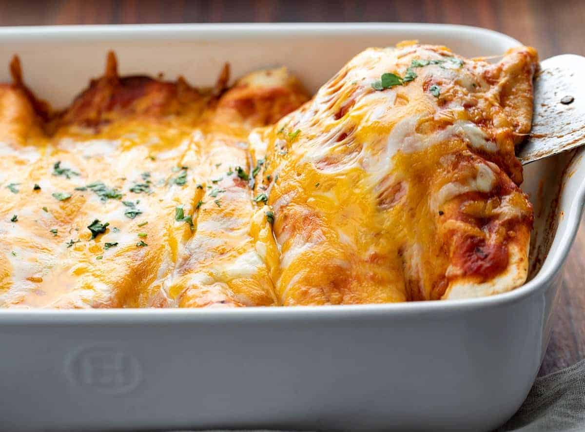 Spatula lifting up a cooked Chicken Enchilada from casserole dish