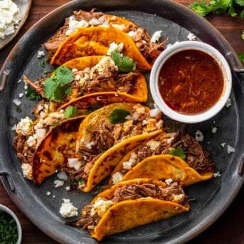 plate of 6 shredded beef tacos with fixings and salsa on a plate