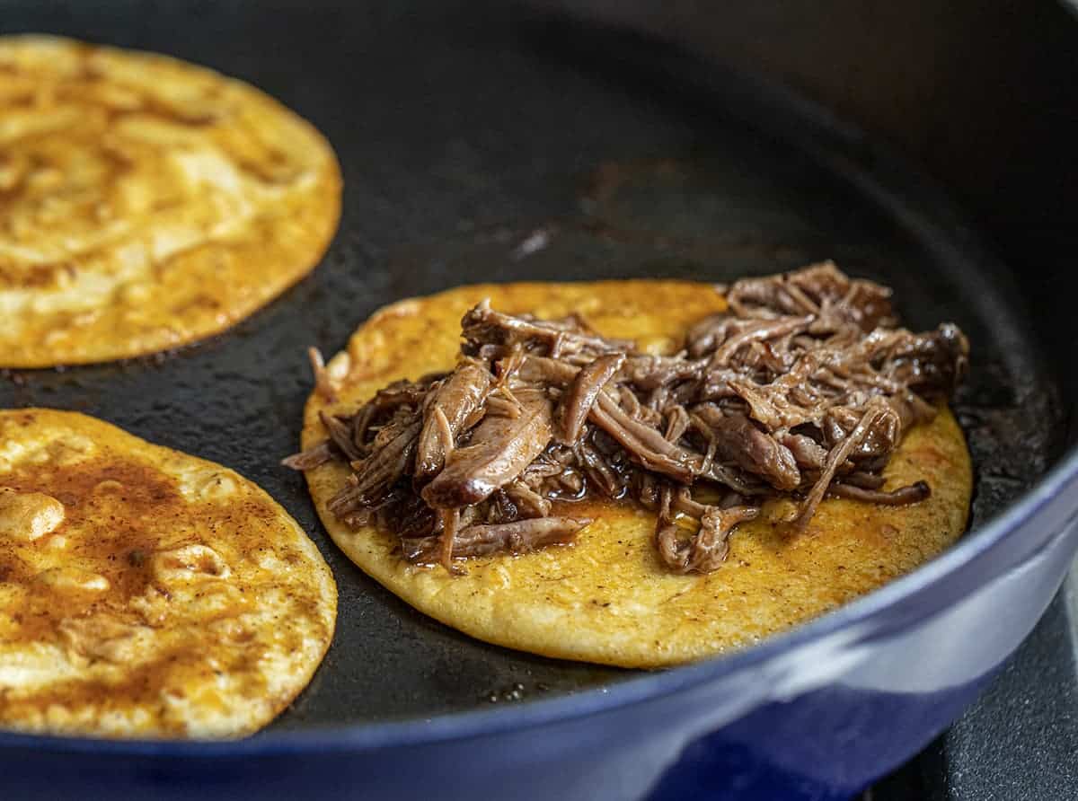 Dipped flour tortillas in a skillet and then adding Slow Cooker Shredded Beef Tacos - Lazy Birria Tacos