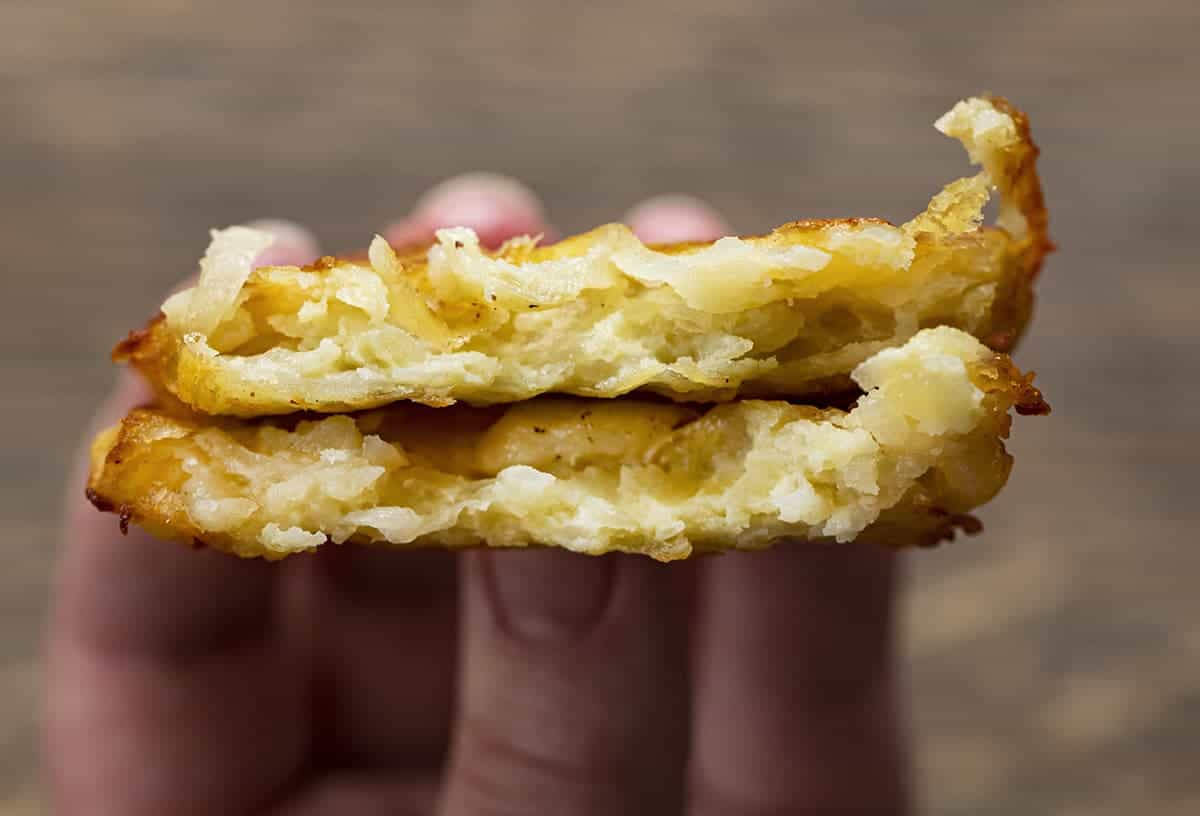 Hand Holding Homemade Hash Brown Patties That is Halved, Showing the Inside Texture.