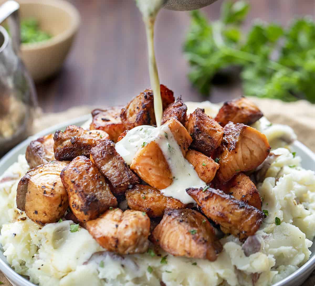 Air Fryer Salmon Bites on Mashed Potatoes with Garlic Sauce Being Poured On Top