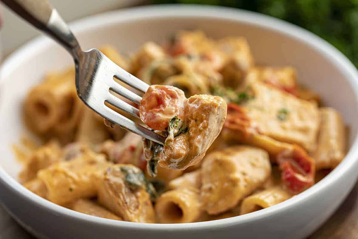 Fork Holding Bite of Tuscan Chicken Pasta in Front of a Bowl