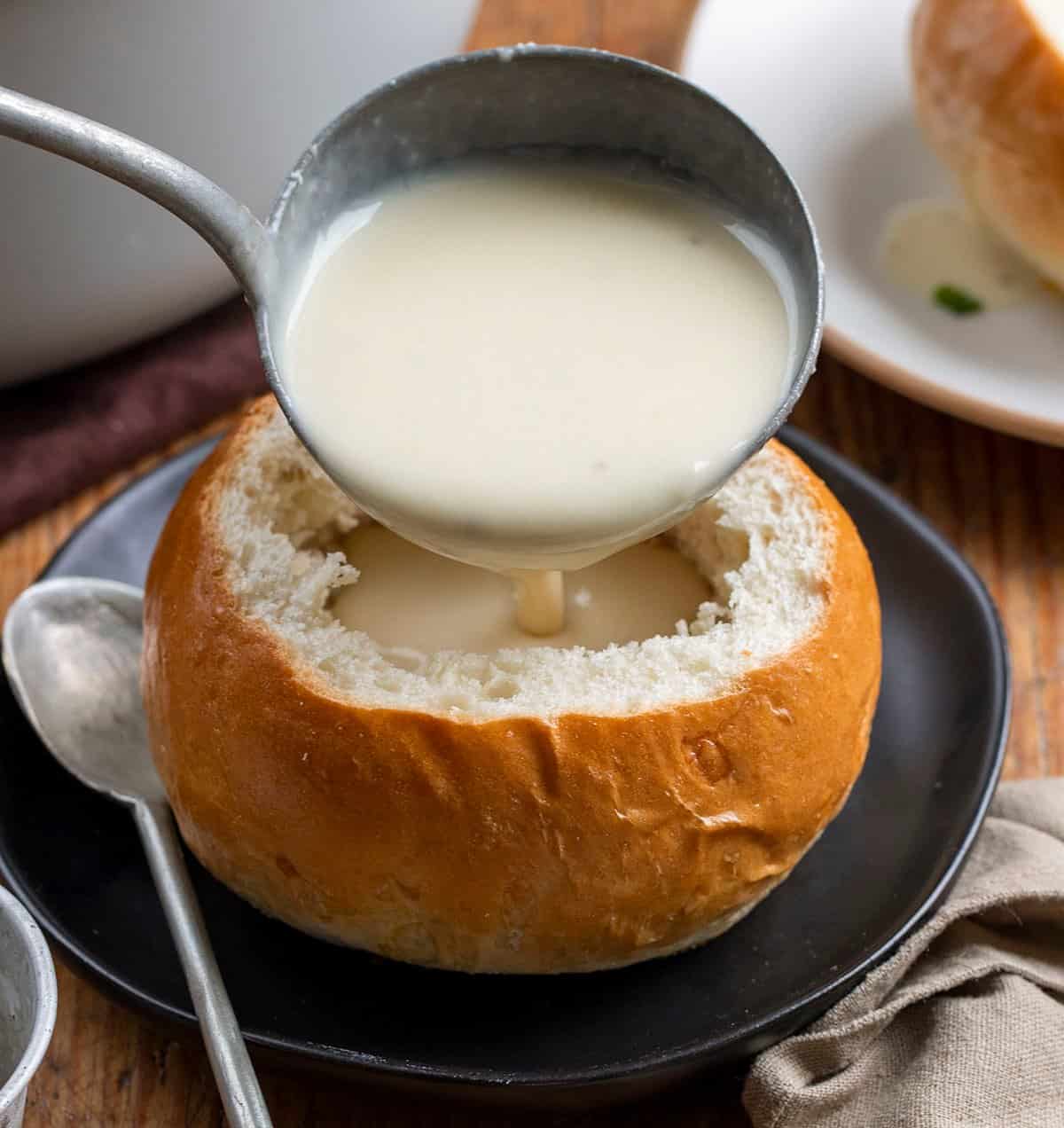 Ladeling 100 Clove Roasted Garlic Soup into a Bread Bowl.