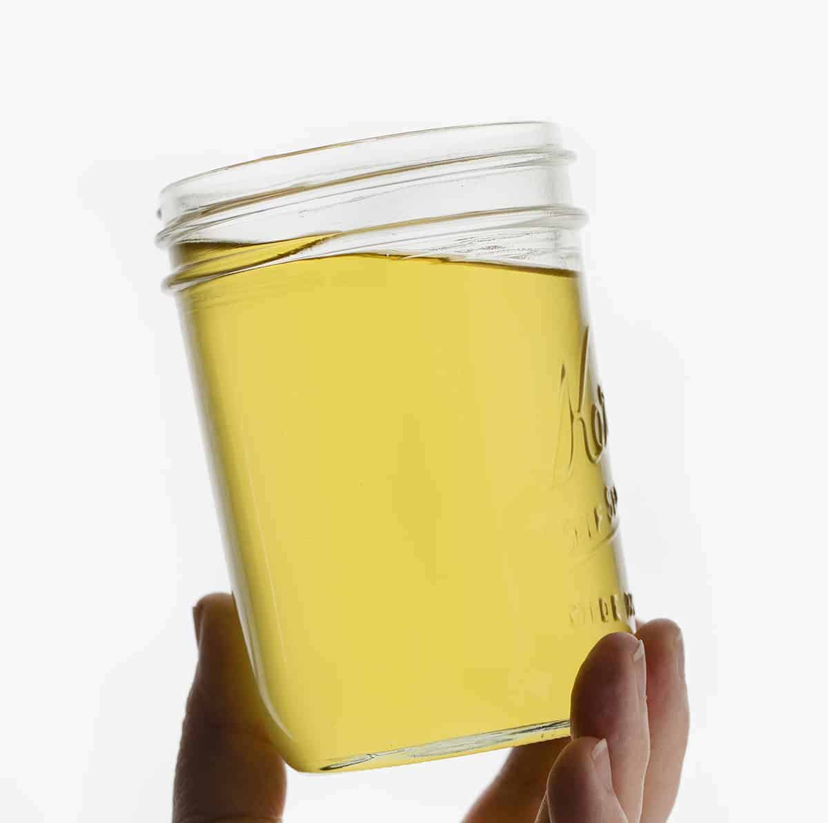 Hand Holding a Jar of Clarified Oil - How to Clean Used Cooking Oil.
