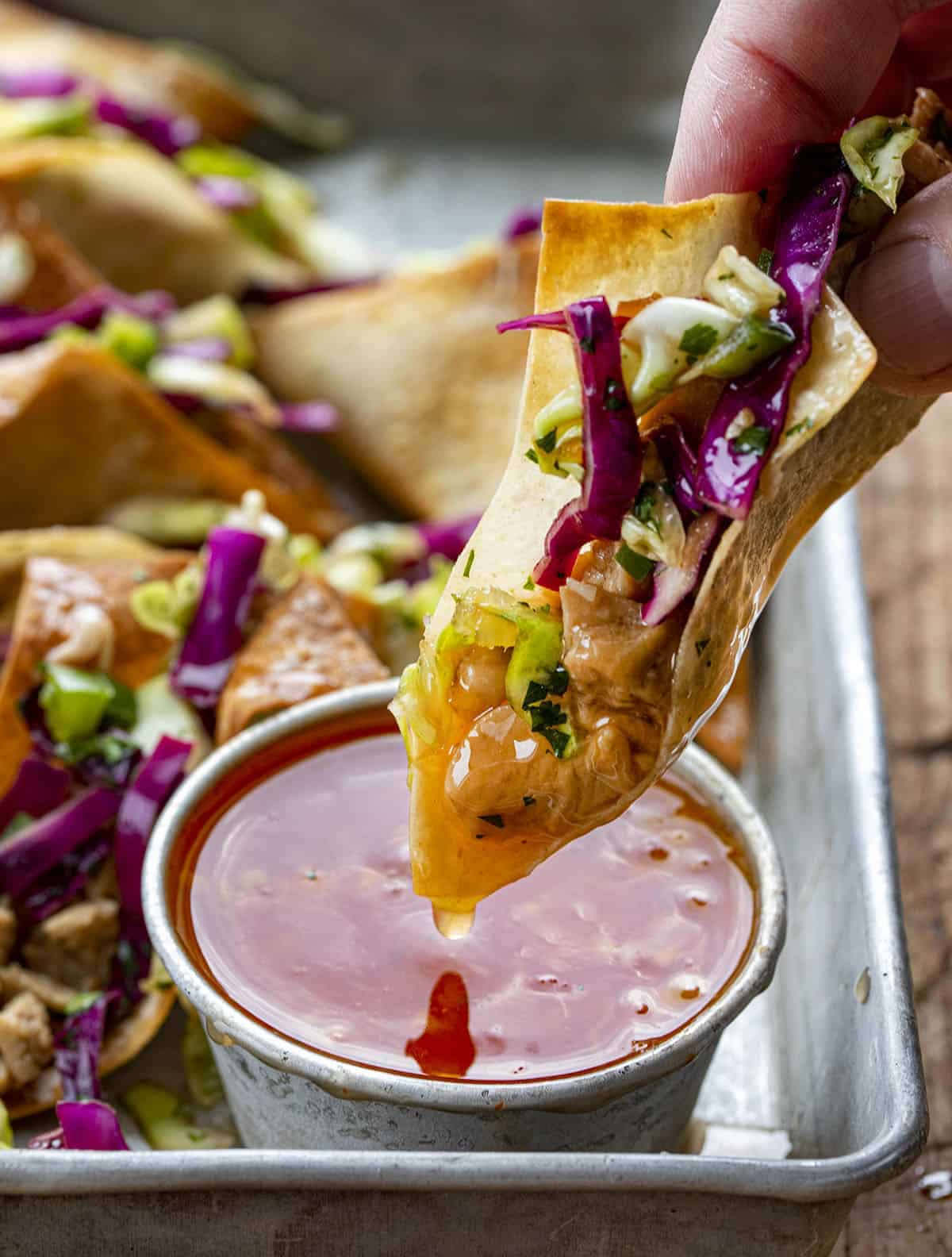Hand Holding a Chicken Wonton Tacos and Dipping It Into Sweet Chili Sauce. 