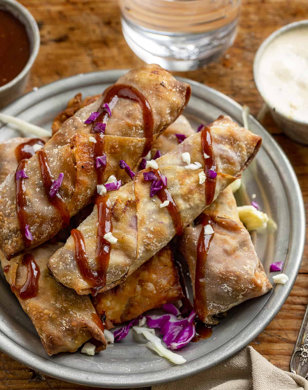 Air Fryer Pulled Pork Egg Rolls Stacked on a Plate and Drizzled with BBQ Sauce
