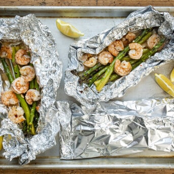 Three Shrimp and Asparagus Foil Packets on a Tray with Two Open.