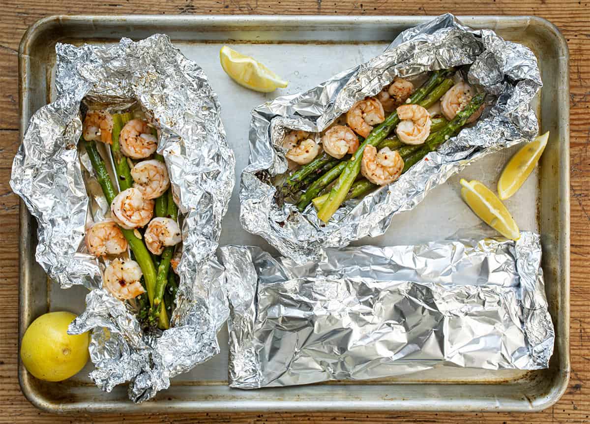 Three Shrimp and Asparagus Foil Packets on a Tray with Two Open
