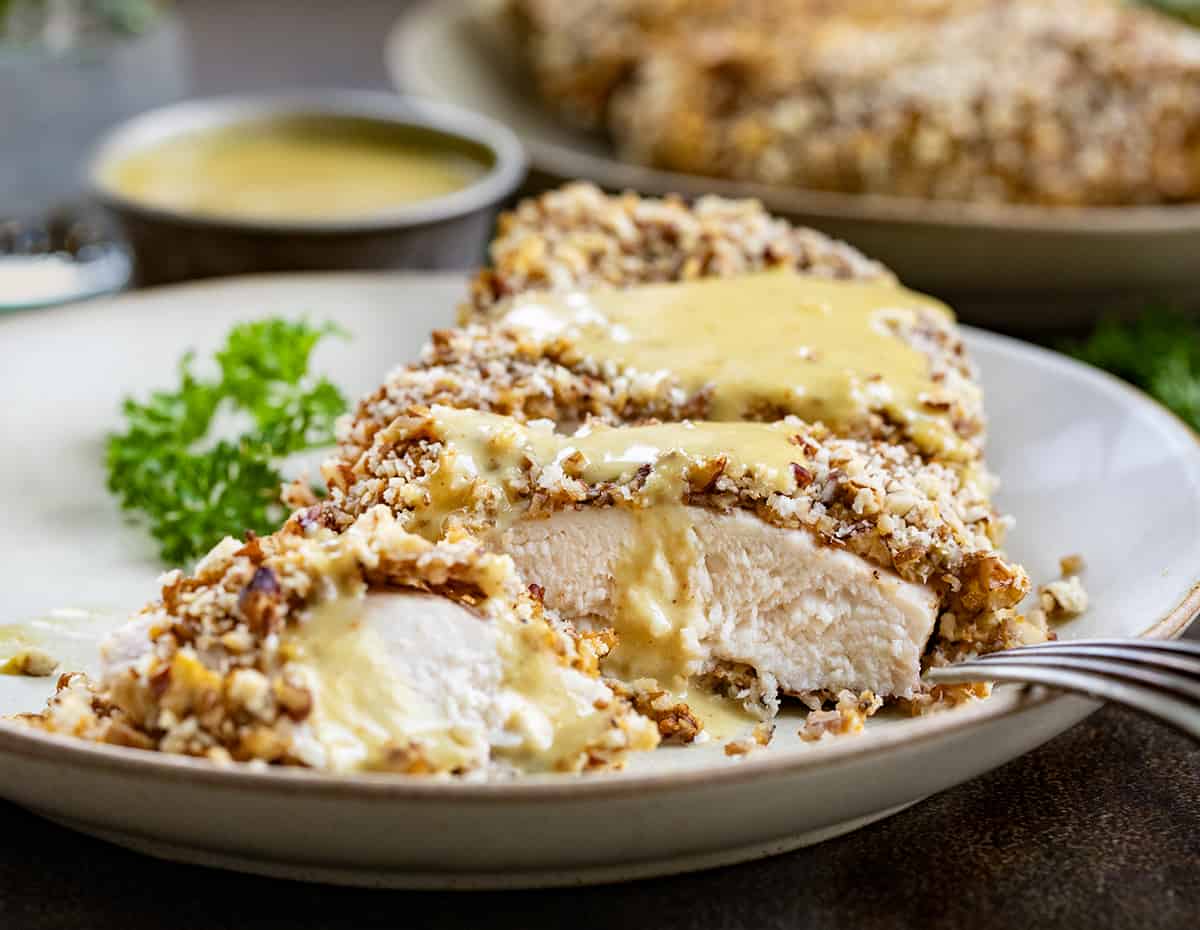 Close up of Pecan Crusted Chicken Cut into Pieces with Sauce on a Plate.