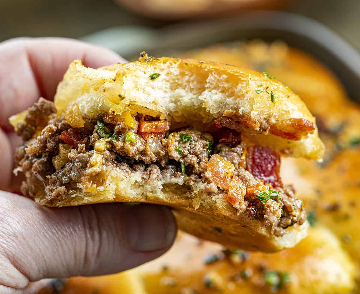 Hand Holding a Bit Into Cowboy Slider Showing Seasoned Ground Beef, Bacon, Jalapeno, and Cheese.