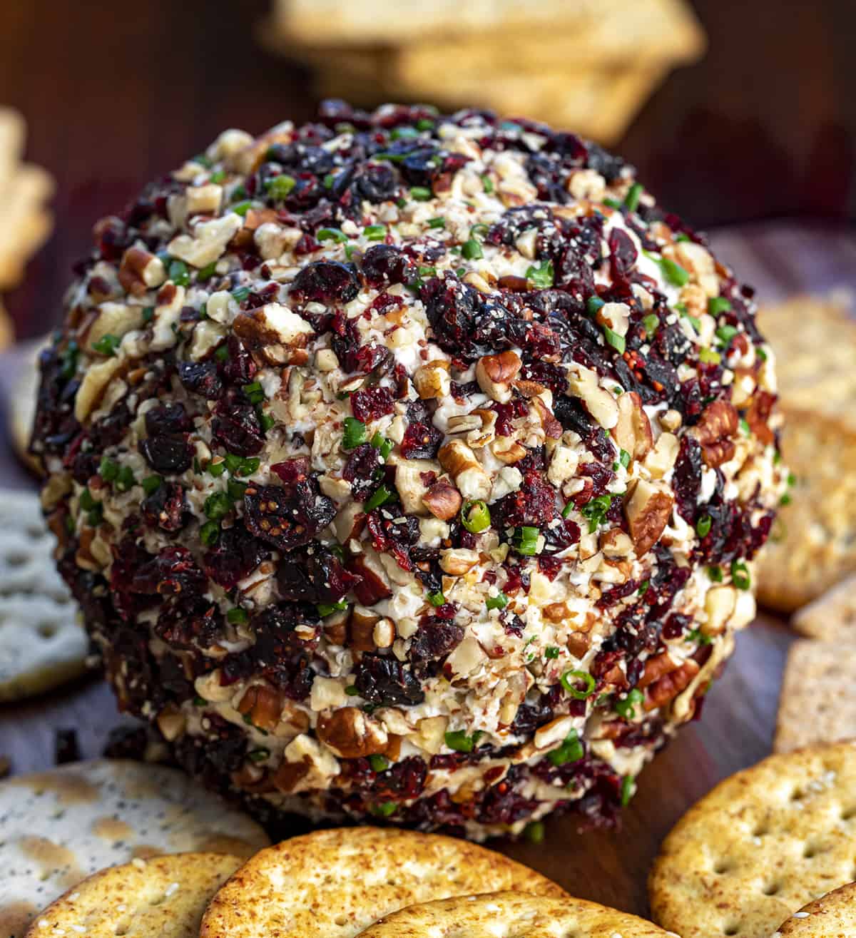 Whole Cranberry Pecan Cheese Ball on a Dark Cutting Board Surrounded by Crackers.