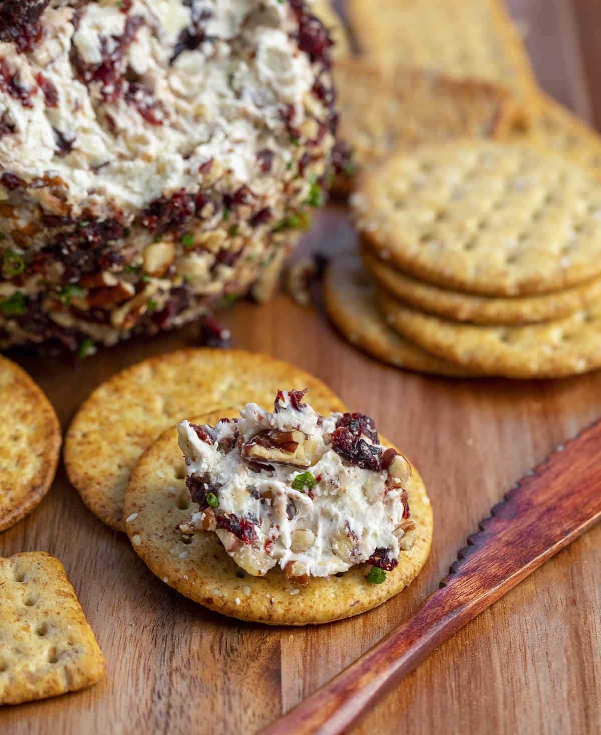 Cranberry Pecan Cheese Ball Spread on a Cracker Next to a Wooden Knife.