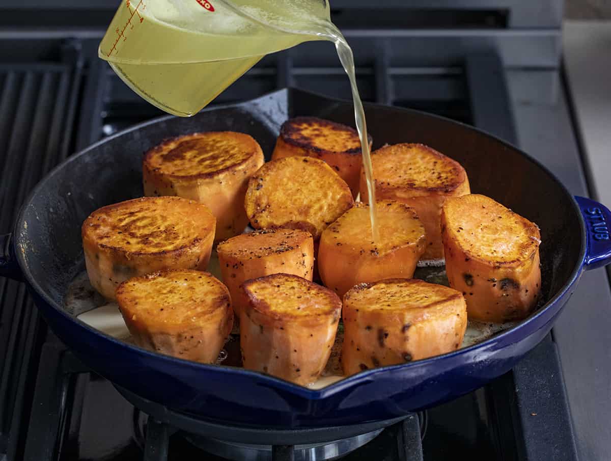 Pouring Chicken Stock Over Peeled and Halved Sweet Potatoes in a Skillet.