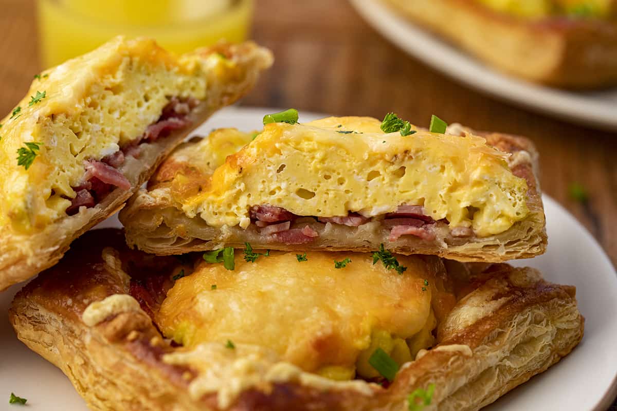 But into Ham and Cheese Breakfast Pastry stacked on a plate with Orange Juice in Background.