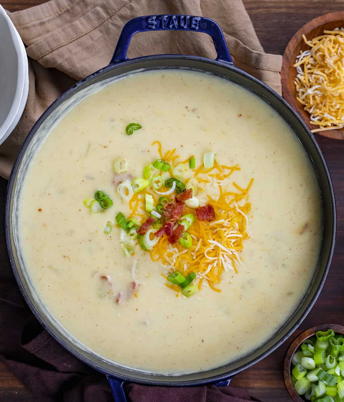 Overhead image of a pot of potato soup on a Cutting board with cheese, green onion, and bacon on top.