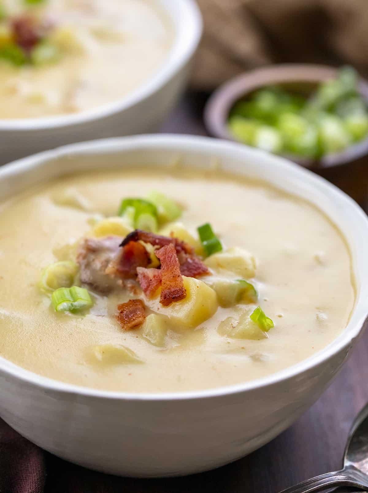 Bowl of Potato Soup with Garnish Next to Another Full Bowl.