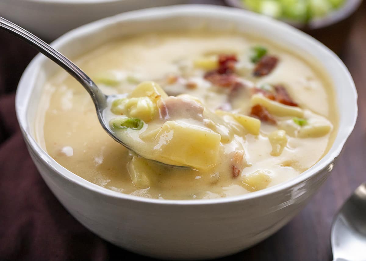 Spoon picking up a full portion of potato soup with big chunks of potato on it.