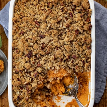 Pan of Sweet Potatoes with Pecan Streusel Topping with Some removed and Spoon Resting in Pan.