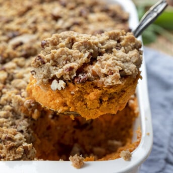 Spoon Taking a Portion from a Pan of Sweet Potatoes with Pecan Streusel Topping.