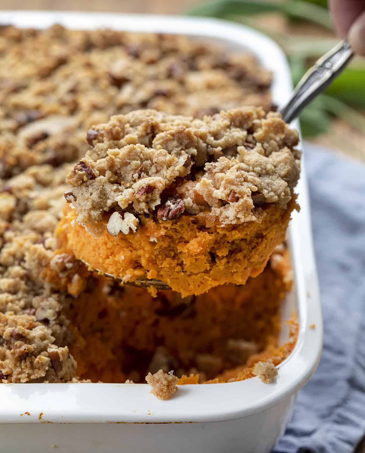 Spoon Taking a Portion from a Pan of Sweet Potatoes with Pecan Streusel Topping.