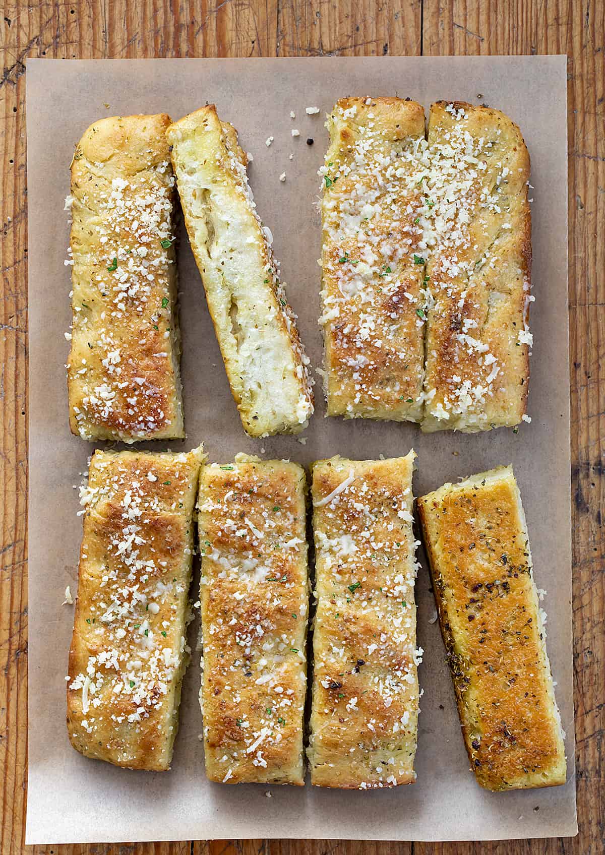 Focaccia Breadsticks on a Piece of Parchment Paper with a Couple of Pieces Flipped Showing the Side and Bottom Texture.