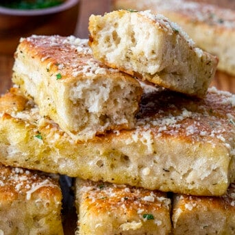 Stacks of Focaccia Breadsticks on a Cutting Board with Pieces Ripped in Half Showing Inside Texture.